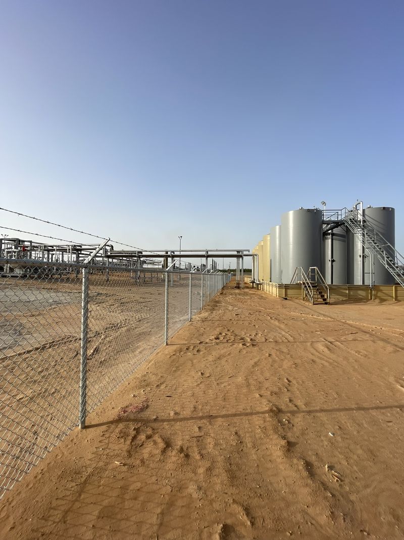 Chain link fence topped with barbed wire running along an industrial tank site