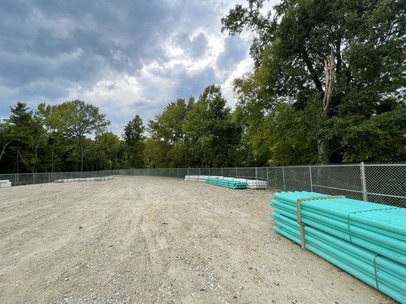 Chain link fence surrounding a gravel yard stacked with bundles of pipe