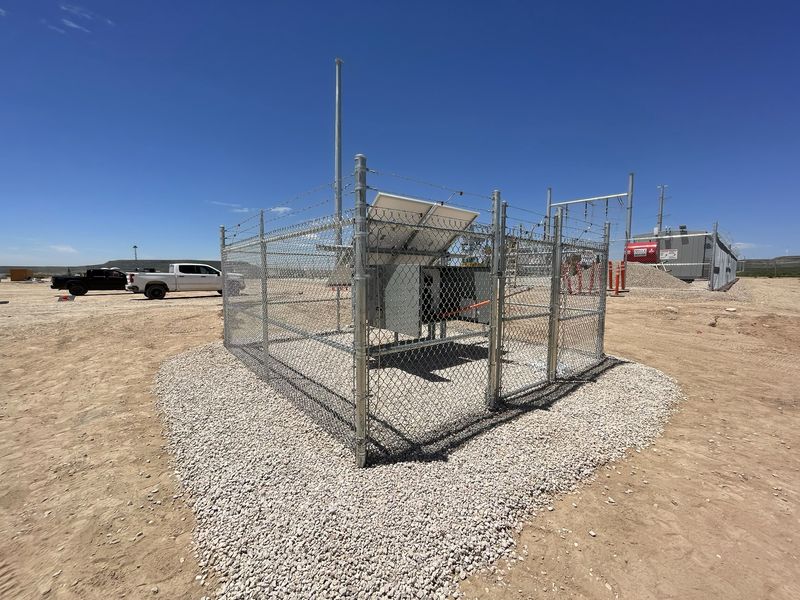Chain link enclosure with barbed wire and a gate around electrical equipment on a gravel pad